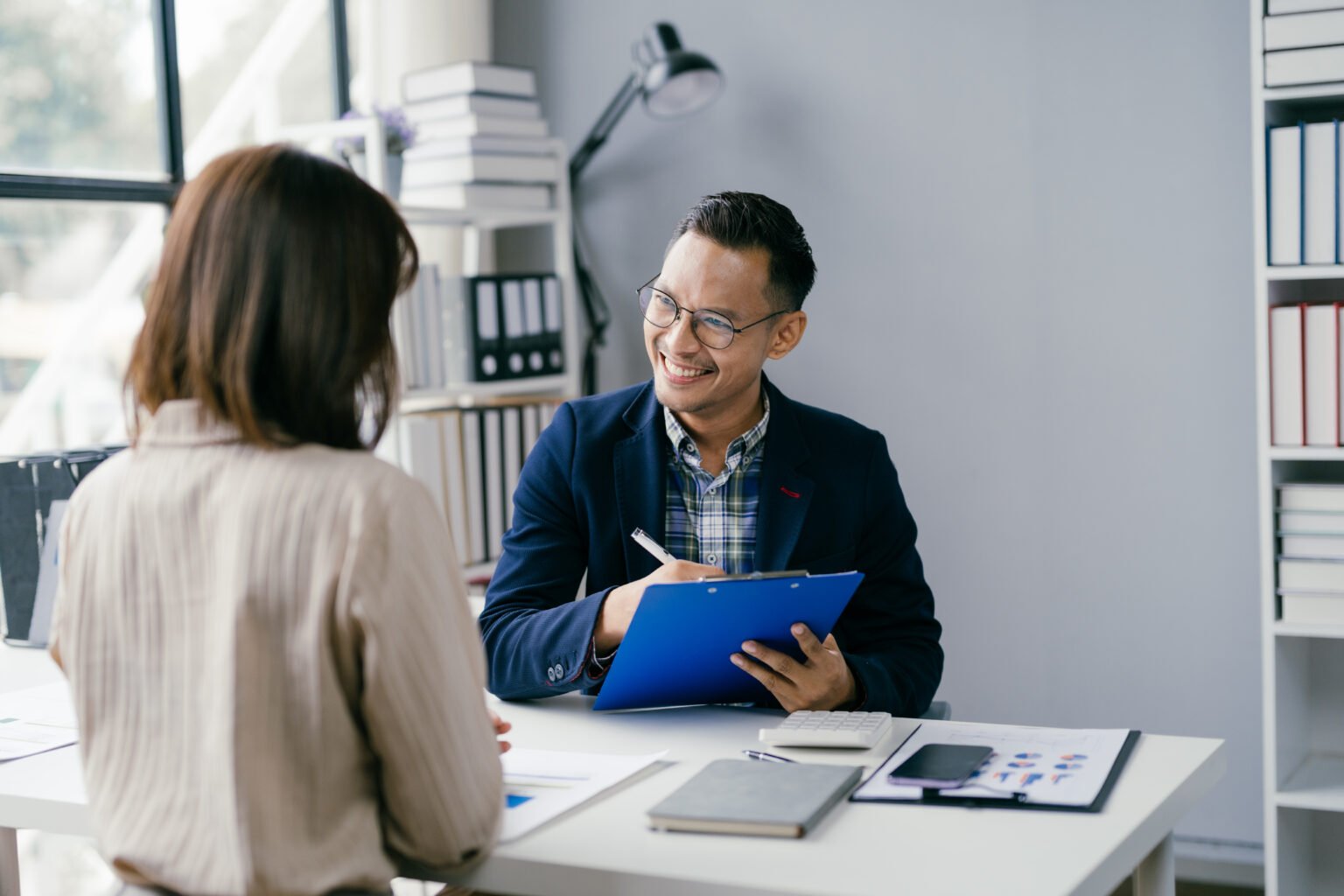 business meeting in modern office with smiling professional holding clipboard and discussing documents
